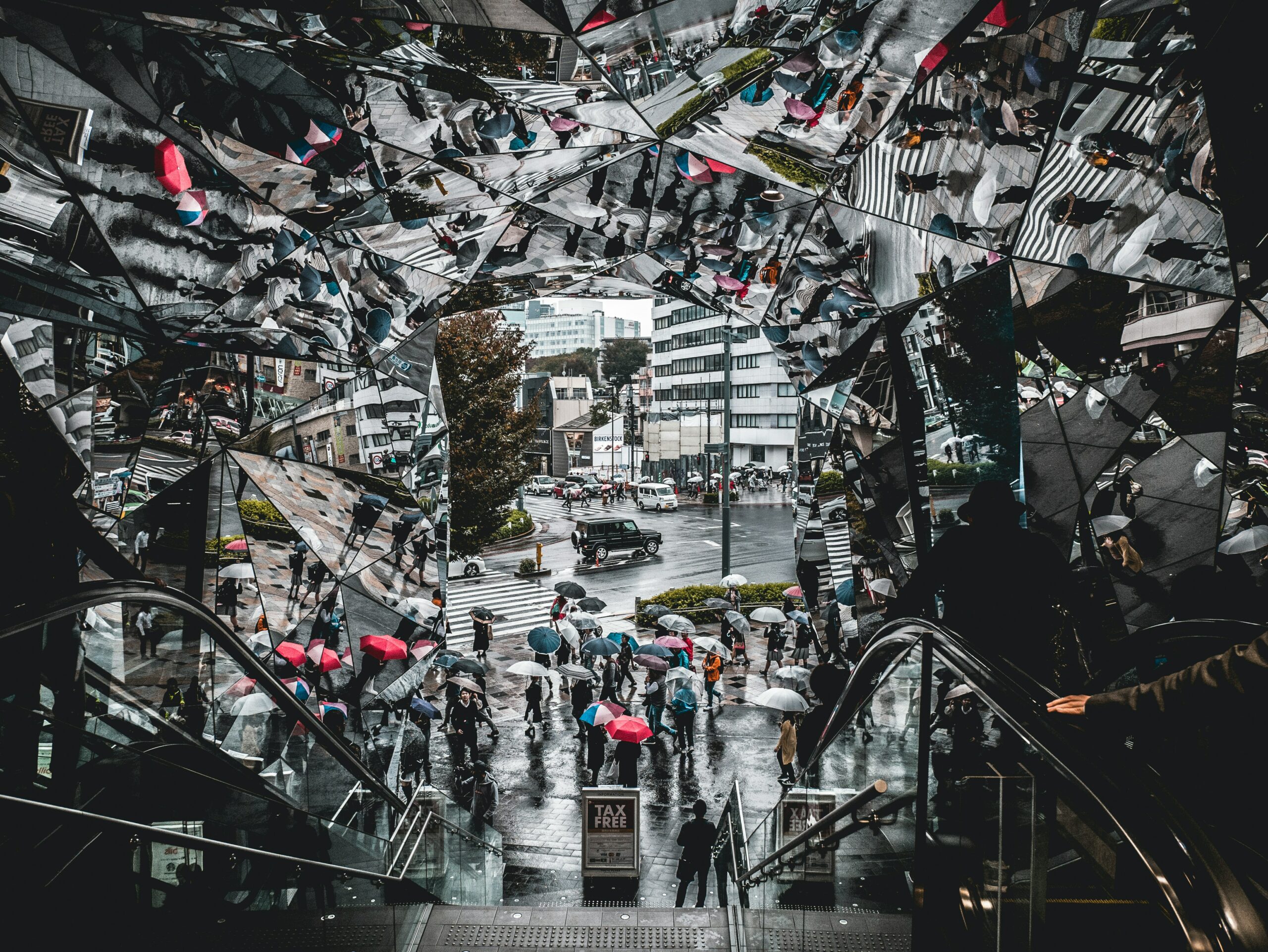 It's an image of a crowd of pedestrians passing by in the pouring rain as this surreal mirror surrounds the setting, giving multiple angles and perspectives.